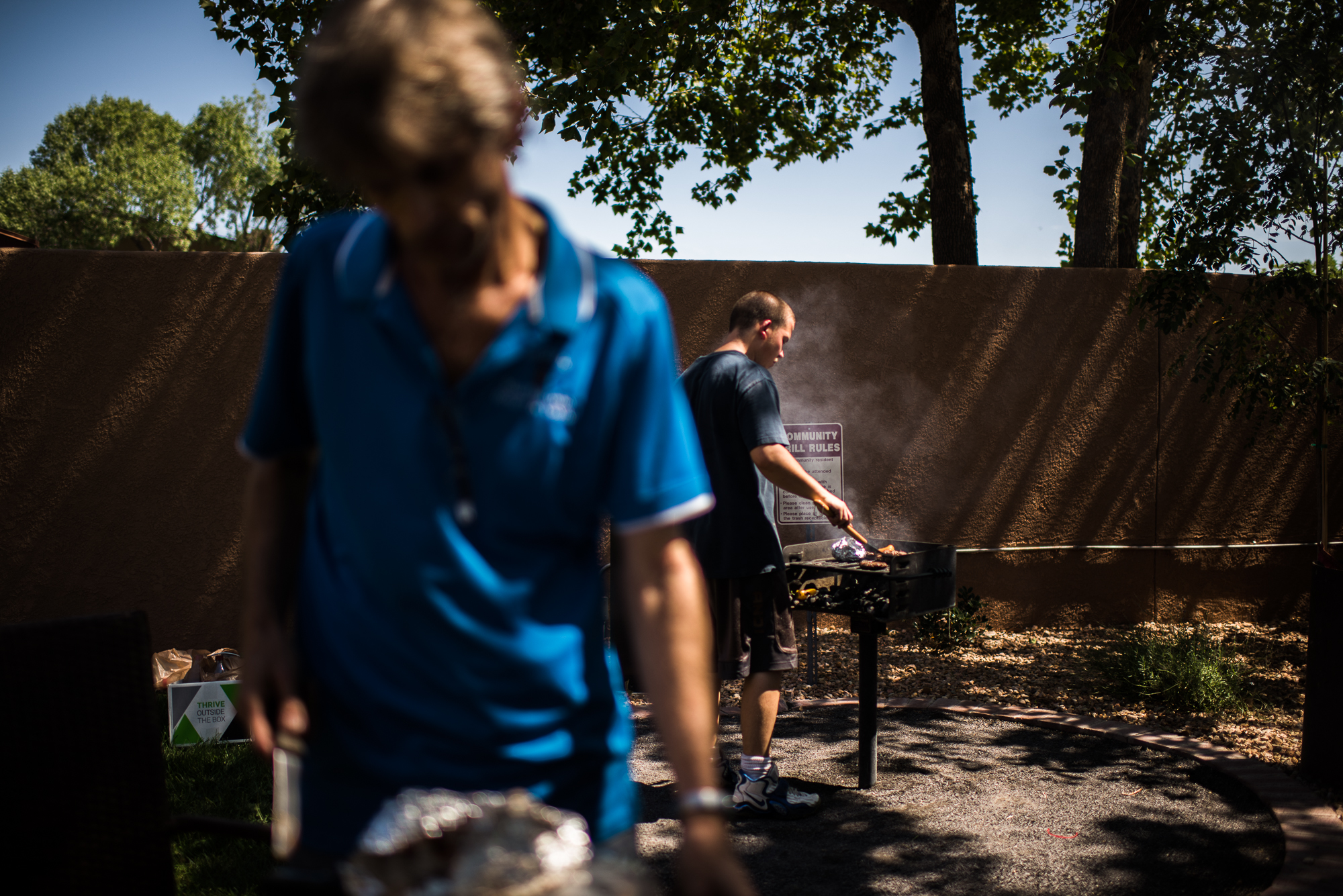 Vinny, age 18, grills meat while a family friend, Jerry, prepares the lunch table in the recreation area of the apartment complex where Jerry lives, 2017.