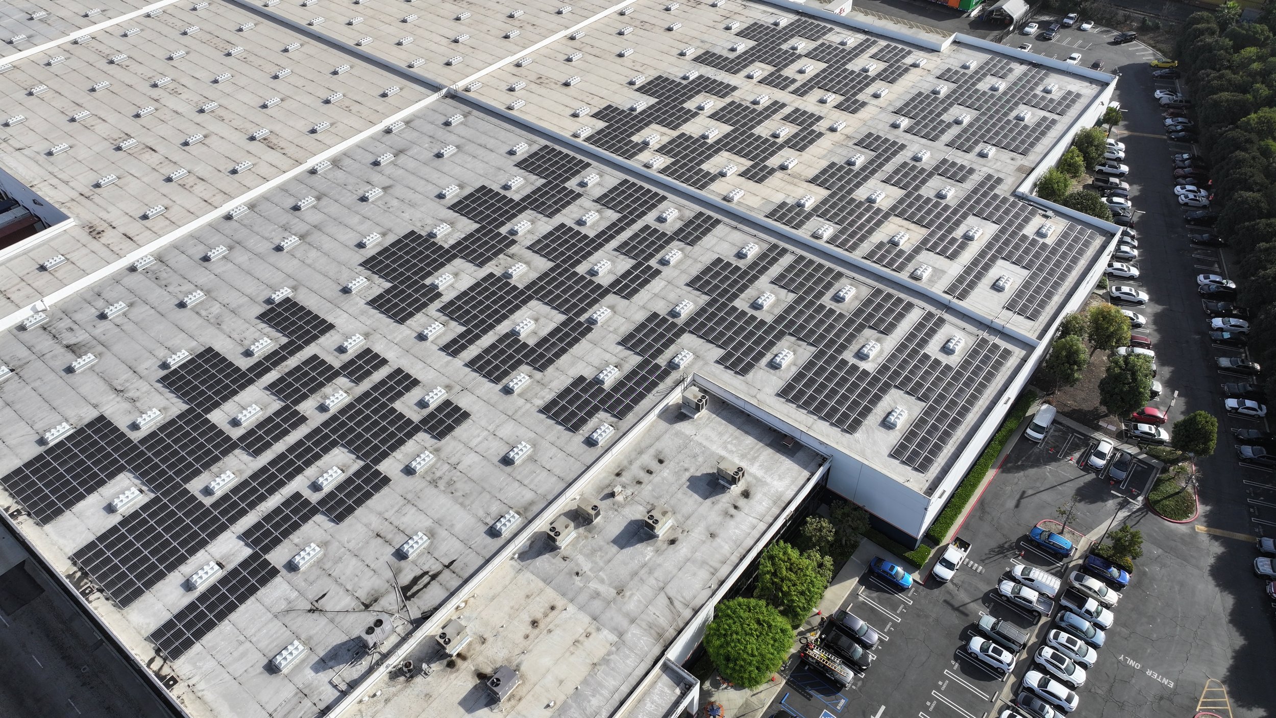 Aerial drone view of a commercial warehouse rooftop in Carson, California, featuring freshly cleaned solar panel arrays. This large-scale solar maintenance project was completed by Guru Solar Cleaning using deionized water and commercial-grade equipm
